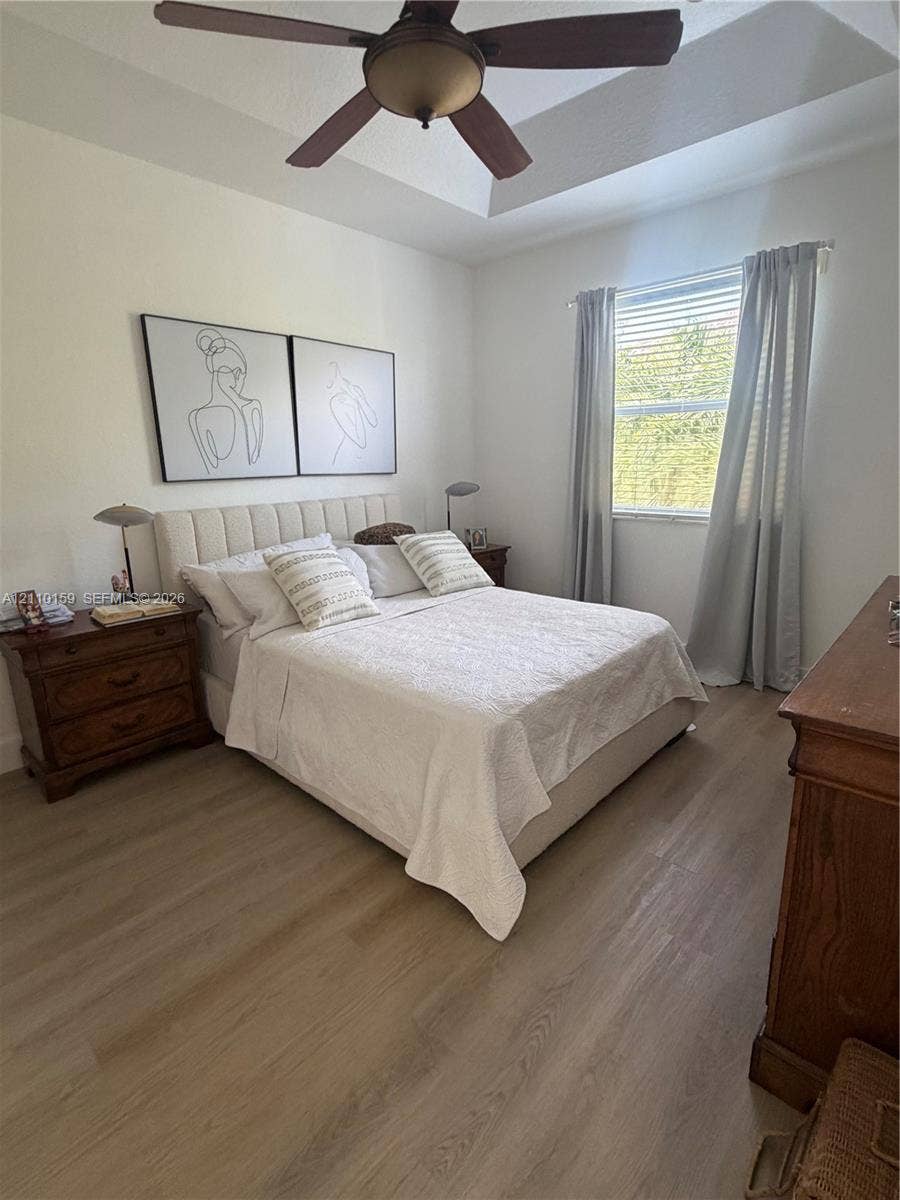 Tray ceiling with a central ceiling fan and wood-finish flooring
