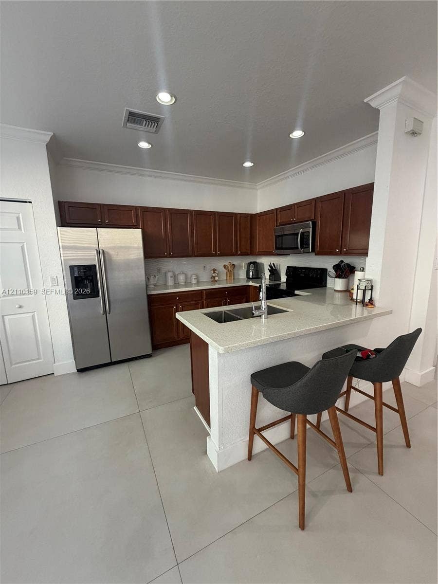 Kitchen featuring stained wood cabinetry, stone-finish countertops, stainless steel refrigerator, recessed lighting, and a breakfast bar