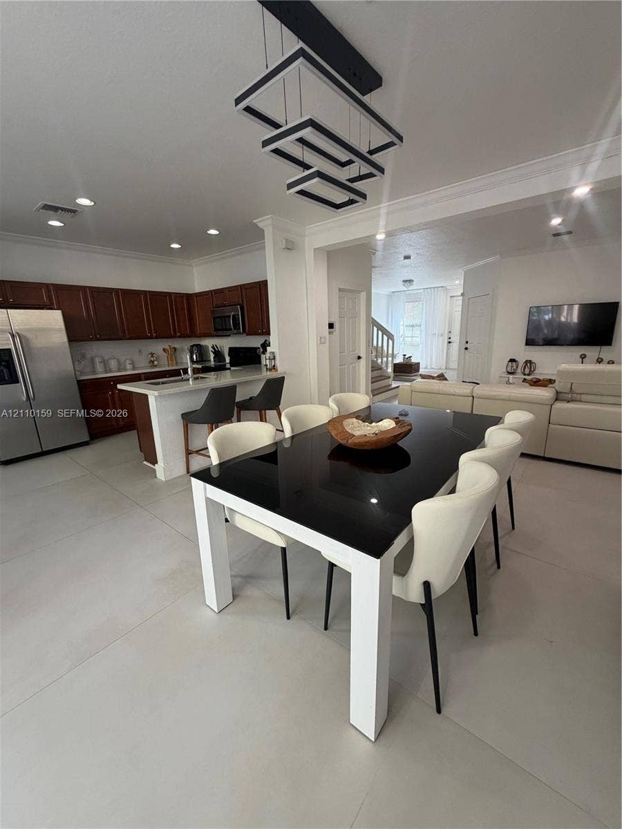 Open-concept kitchen featuring dark wood cabinetry, an expansive island with a white countertop, large-format tile flooring, recessed lighting, and a geometric modern chandelier