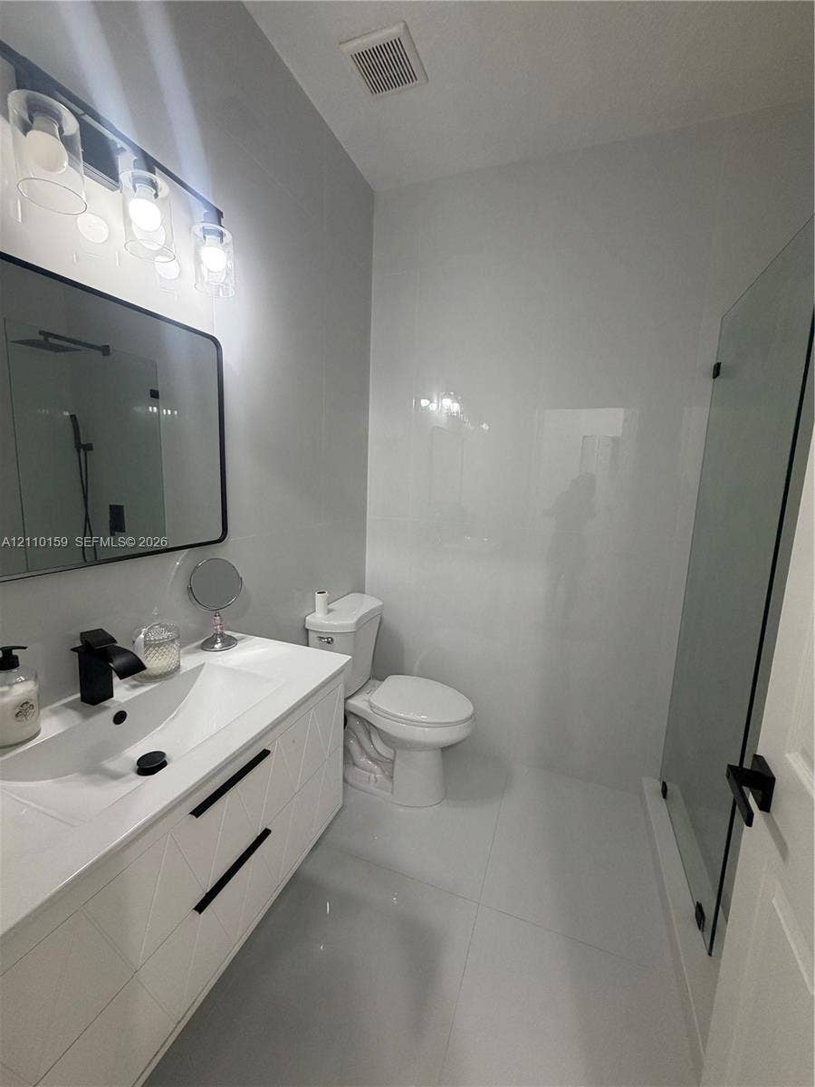 Bathroom featuring a white geometric-pattern vanity, rectangular vessel sink, matte black faucet, wall-mounted rectangular mirror, and glass-enclosed shower