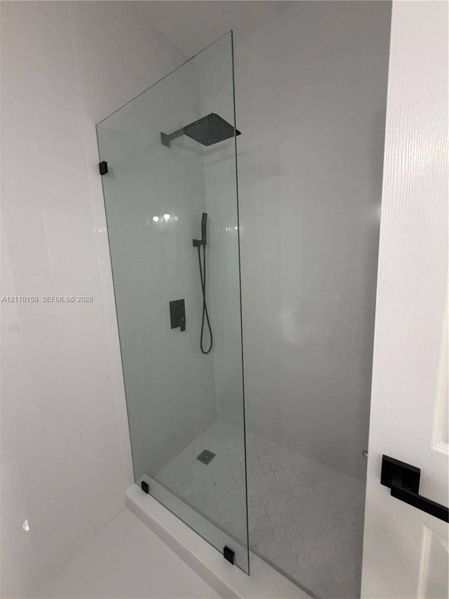 Walk-in shower featuring a frameless glass panel, matte black wall-mounted fixtures, a square rain-style showerhead, and a hand-held sprayer