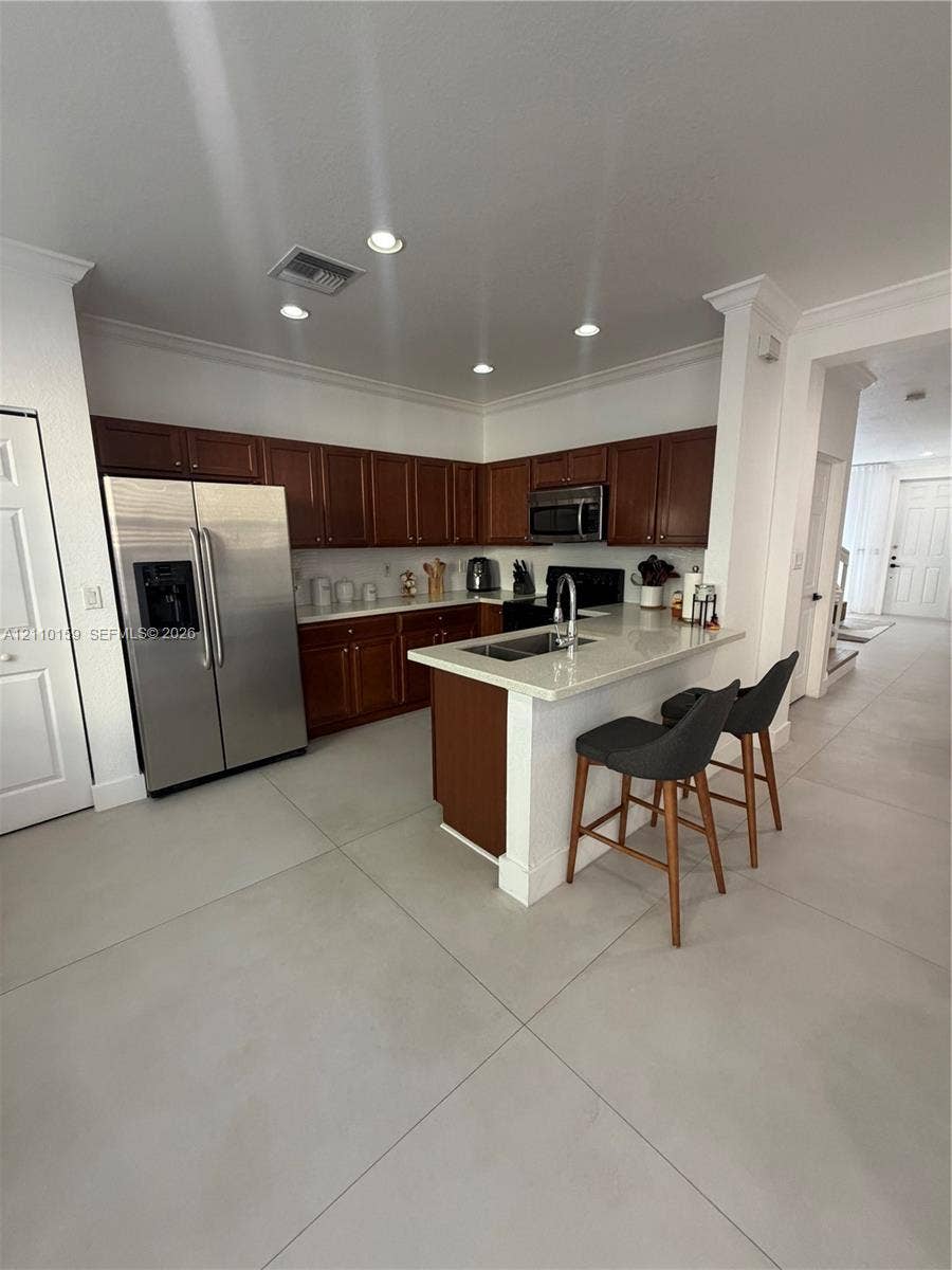 Kitchen featuring dark-toned cabinetry, light-colored countertops, stainless steel appliances, a peninsula with an undermount sink, and recessed lighting