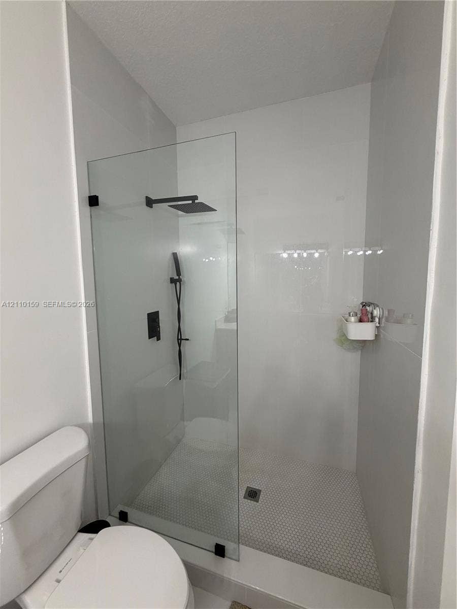 Walk-in shower featuring a frameless glass partition, matte black rainfall showerhead, handheld sprayer, and hexagon tile floor