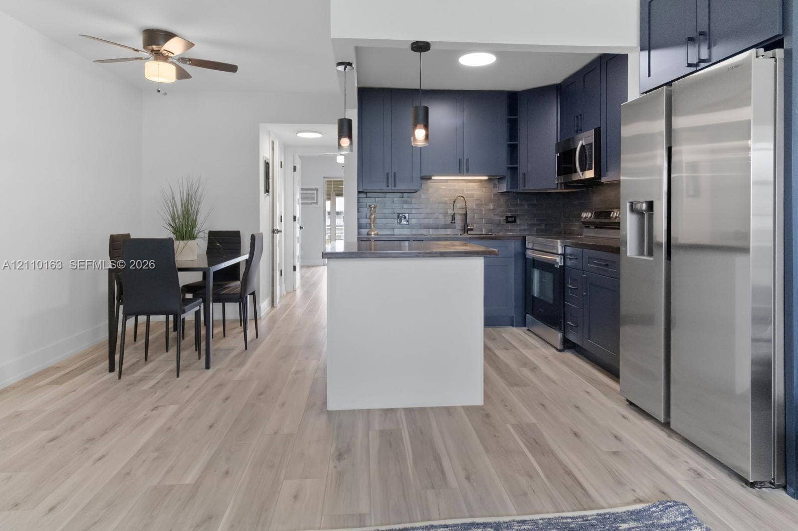 Kitchen featuring dark cabinetry, stainless steel appliances, a white kitchen island, pendant lighting, and wood-finish flooring
