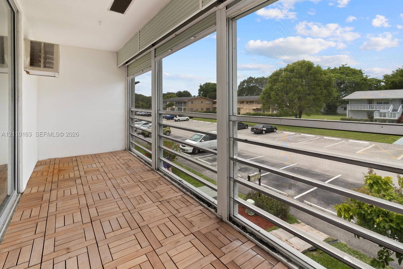 Enclosed balcony featuring wood-finish deck tiling, aluminum-framed sliding windows, and a dedicated wall-mounted climate control unit