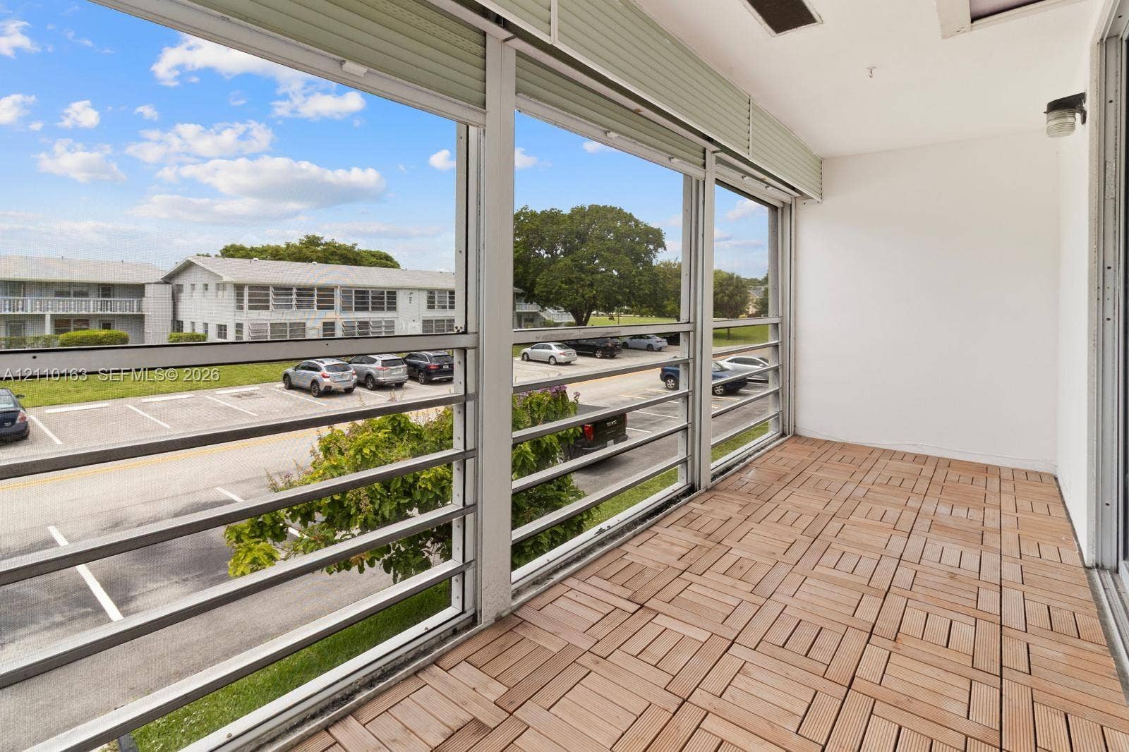 Enclosed balcony featuring wood-finish flooring, metal railing, and retractable overhead shades