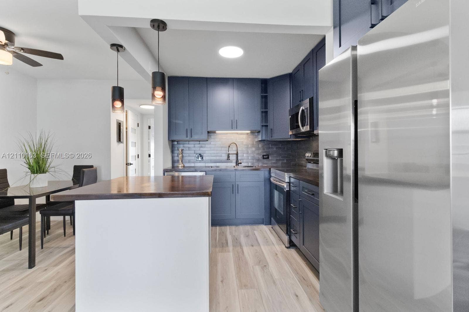 Kitchen featuring dark blue cabinetry, wood-finish island countertop, stainless steel appliances, subway tile backsplash, and cylindrical pendant lighting