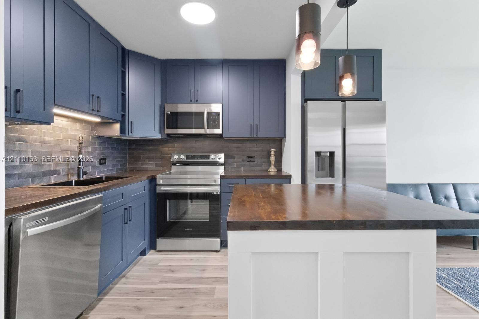Kitchen featuring navy blue cabinetry, wood-finish countertops, stainless steel appliances, brick-style tile backsplash, and a central island with a white base