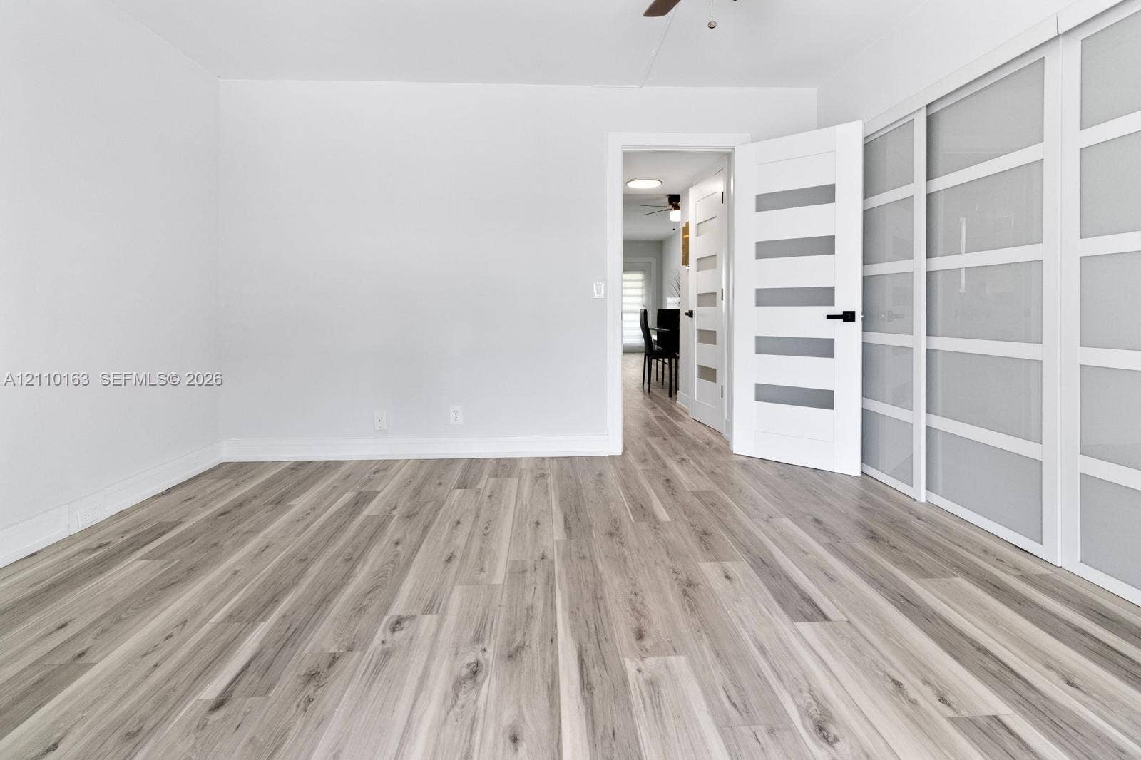 Wood-finish flooring, sliding glass-panel closet doors, and a six-panel door with frosted glass inserts featuring matte black hardware