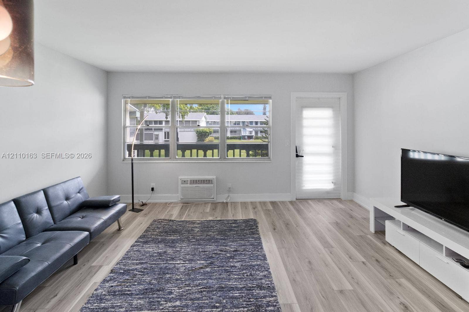 Neutral-toned interior featuring wood-finish flooring, a triple-pane window configuration, and an exterior entry door with integrated blind