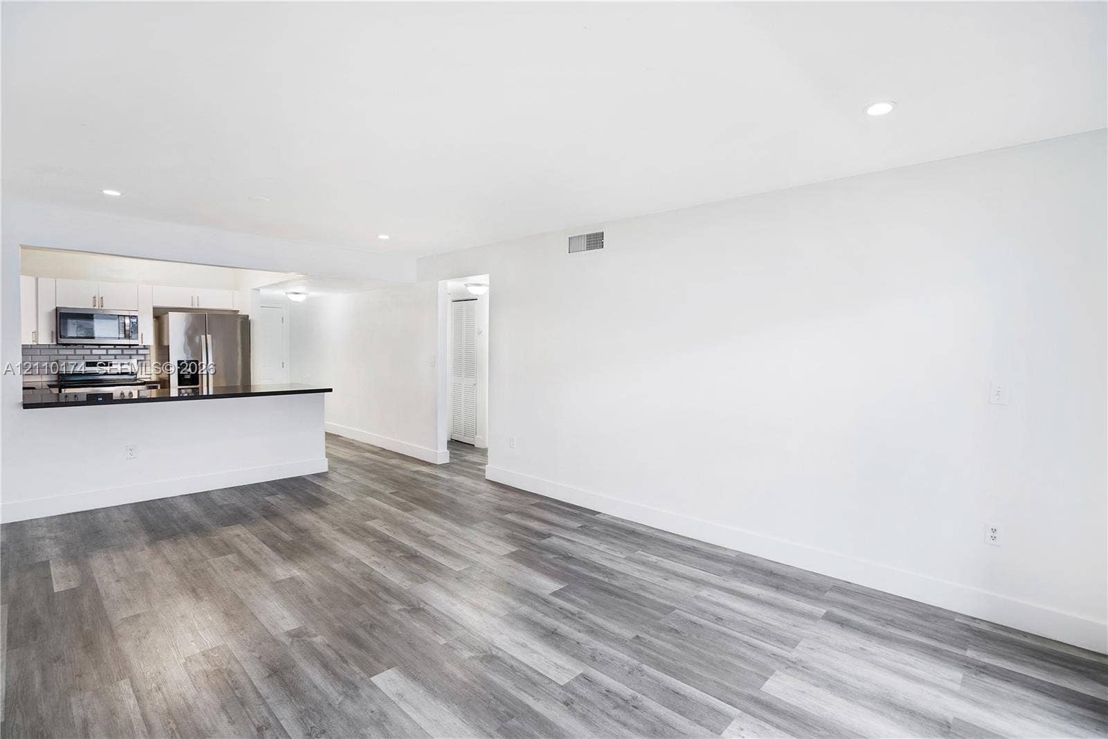 Open-concept interior featuring wood-finish flooring, recessed lighting, and a kitchen peninsula with a dark countertop and white cabinetry