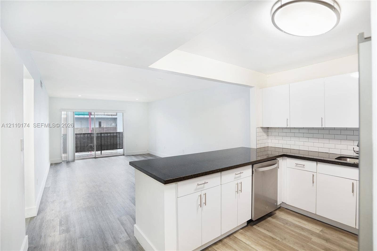 Kitchen featuring white cabinetry, dark countertops, subway tile backsplash, stainless steel dishwasher, and wood-finish flooring
