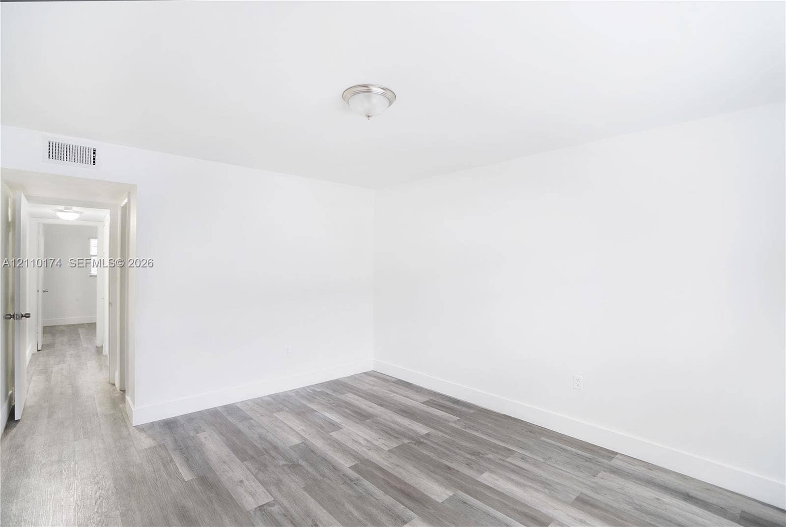 Room interior featuring wood-finish flooring, white walls, and a ceiling-mounted light fixture