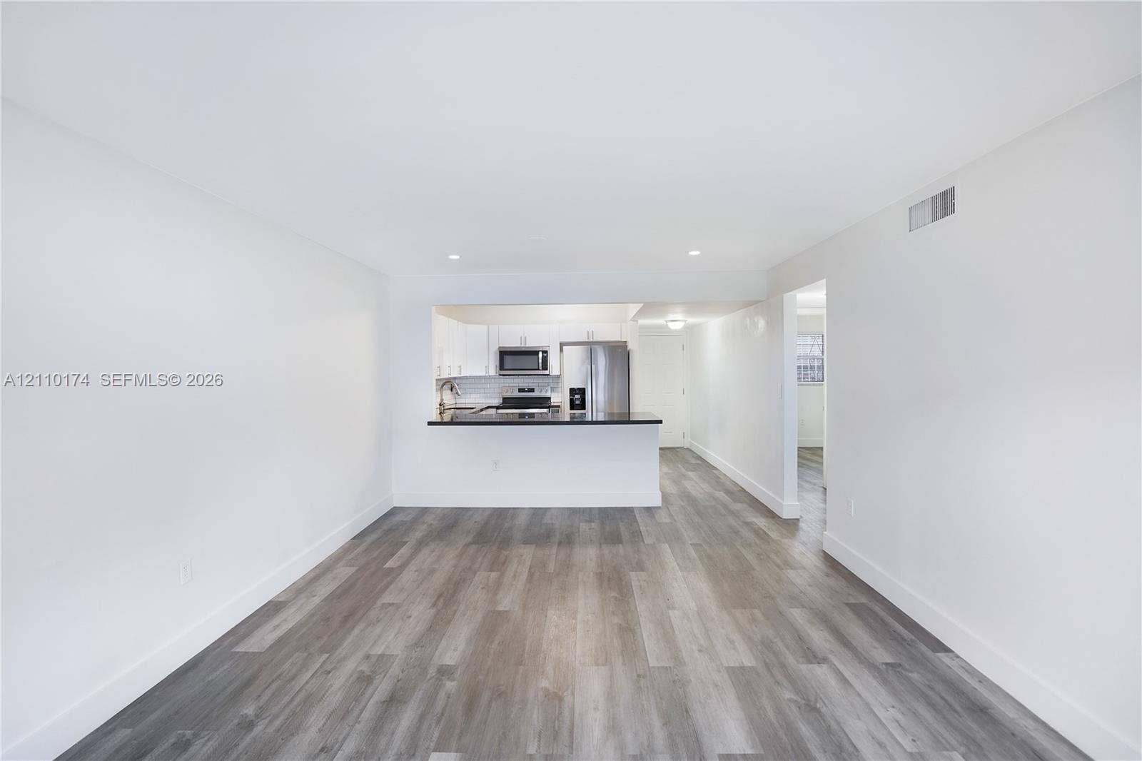 Open-concept interior featuring wood-finish flooring, white cabinetry, dark countertops, and stainless steel kitchen appliances