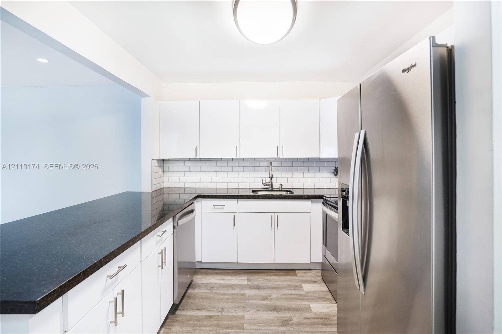 Kitchen featuring white flat-panel cabinetry, dark stone-finish countertops, stainless steel appliances, a white subway tile backsplash, and wood-finish flooring
