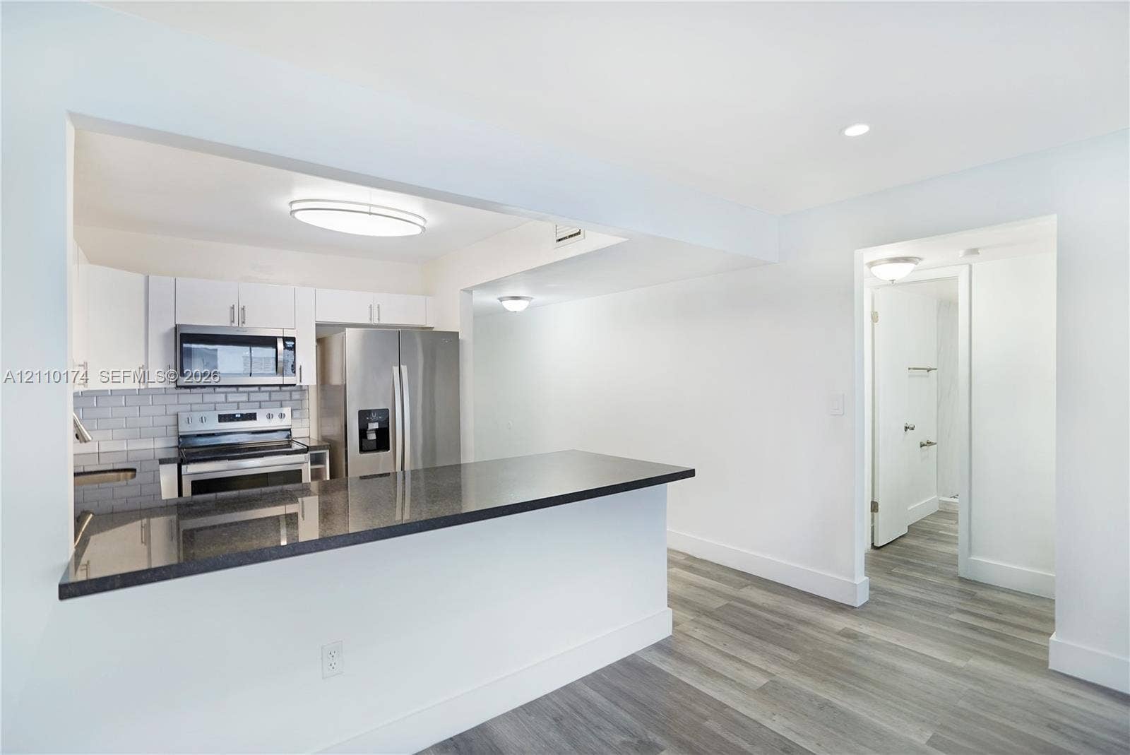 Kitchen featuring a dark stone countertop peninsula, white shaker-style cabinetry, stainless steel appliances, grey subway tile backsplash, and wood-finish flooring