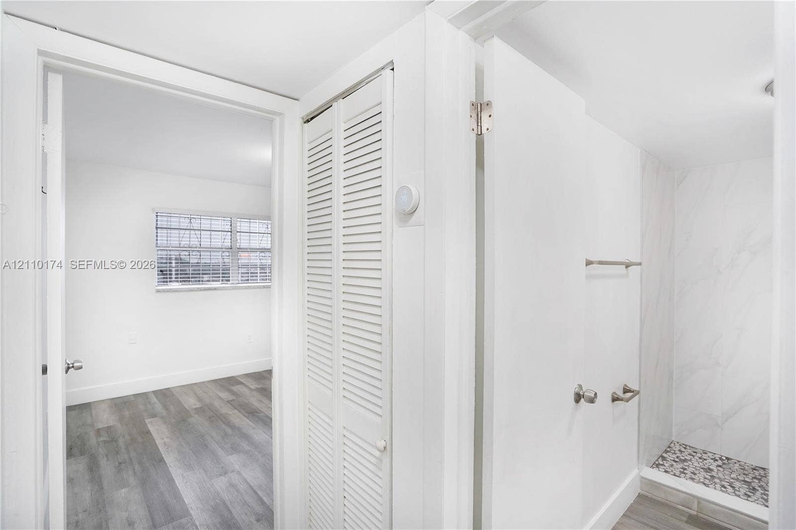 Walk-in shower with stone-finish tile surround and pebble-texture flooring, white louvered closet doors, and wood-finish flooring