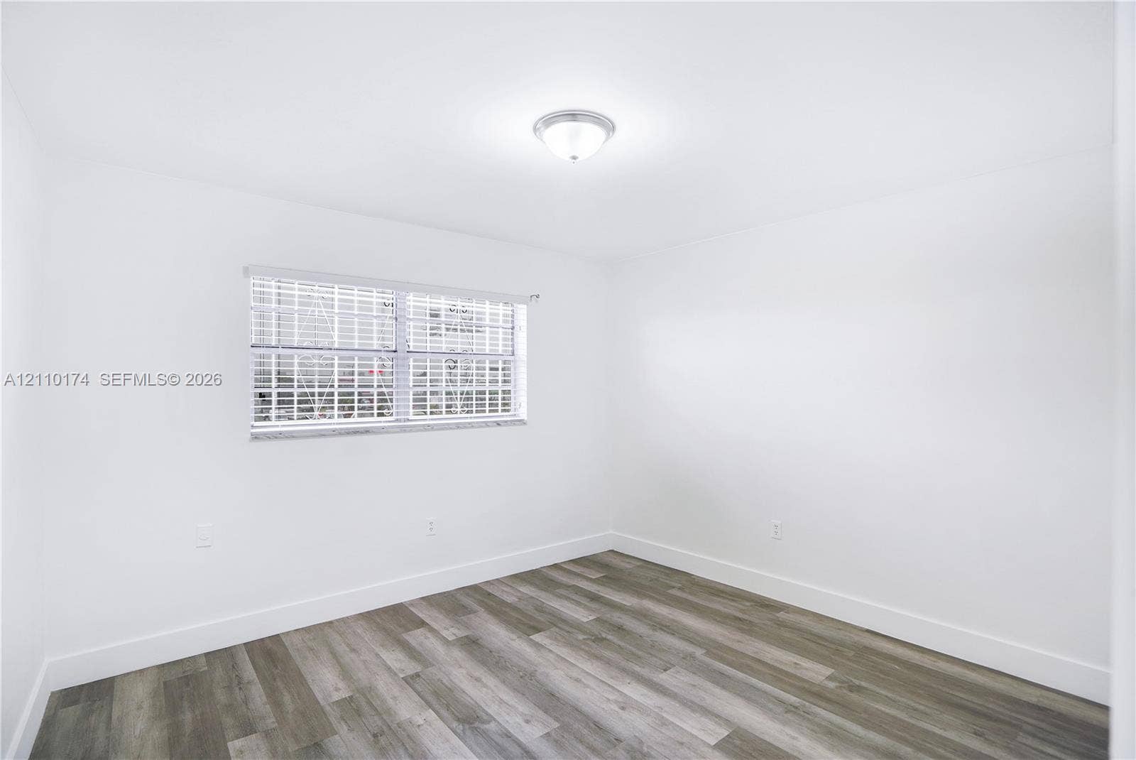 Interior space featuring wood-finish flooring, white walls, a flush-mount ceiling light fixture, and a single window with horizontal blinds