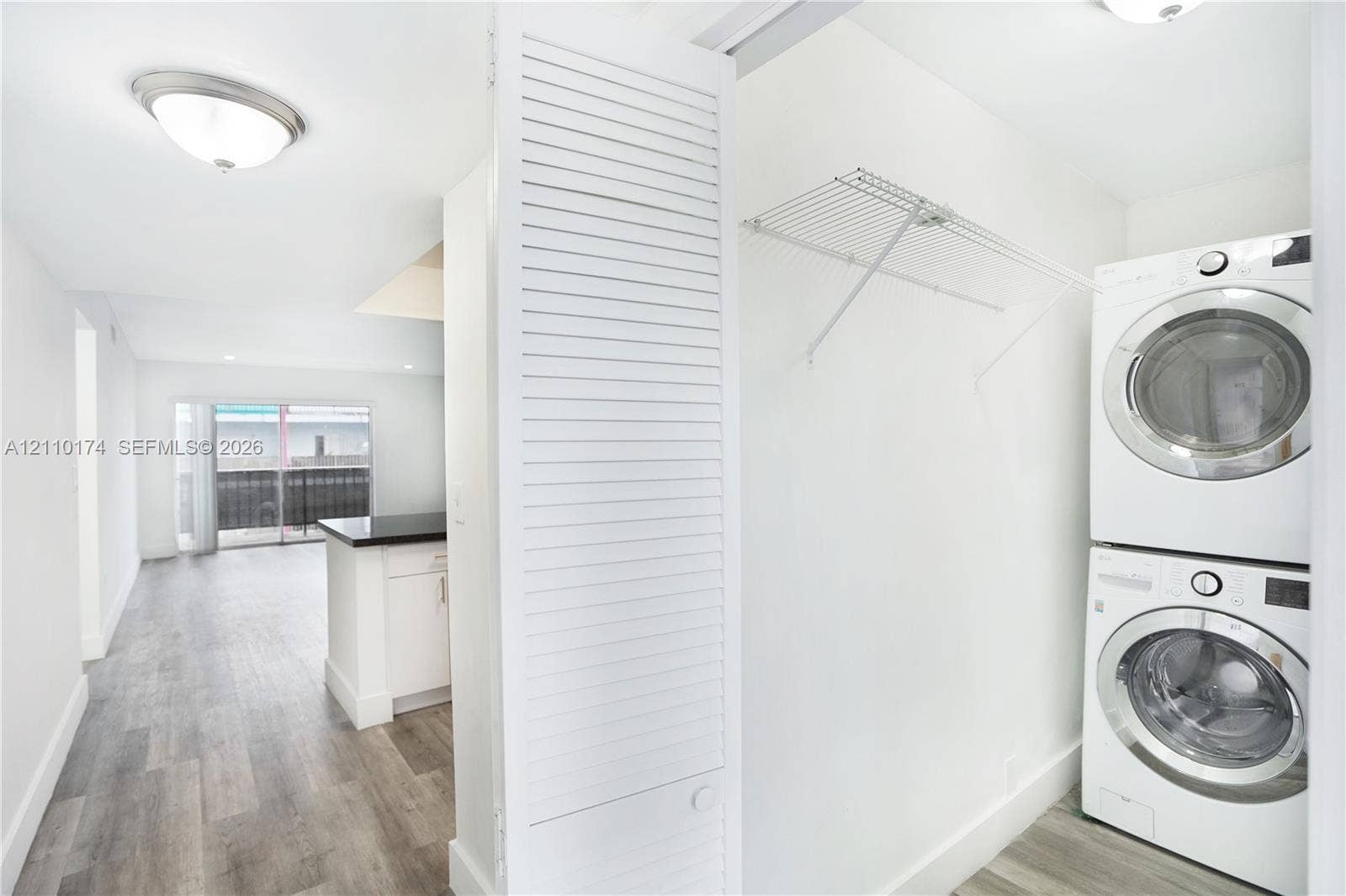 Laundry area featuring a stacked washer and dryer unit, integrated wire shelving, wood-finish flooring, and a louvered bi-fold door