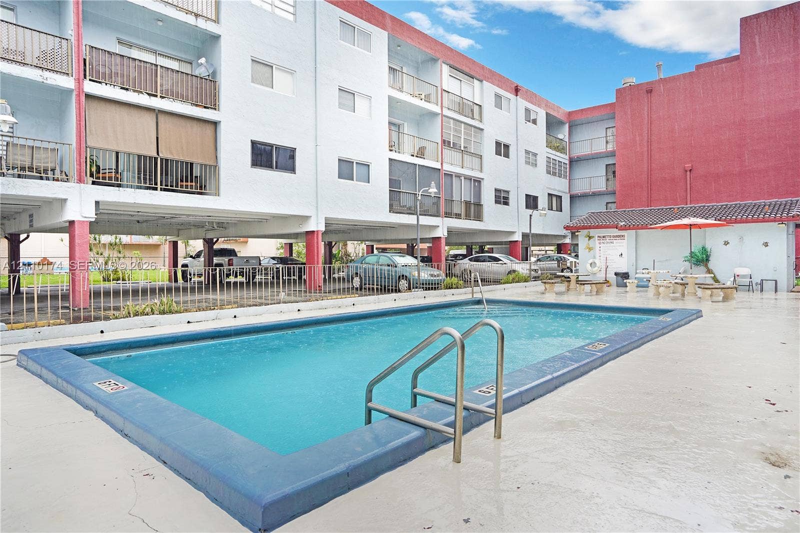In-ground swimming pool featuring a concrete deck, metal handrails, and a nearby covered pavilion
