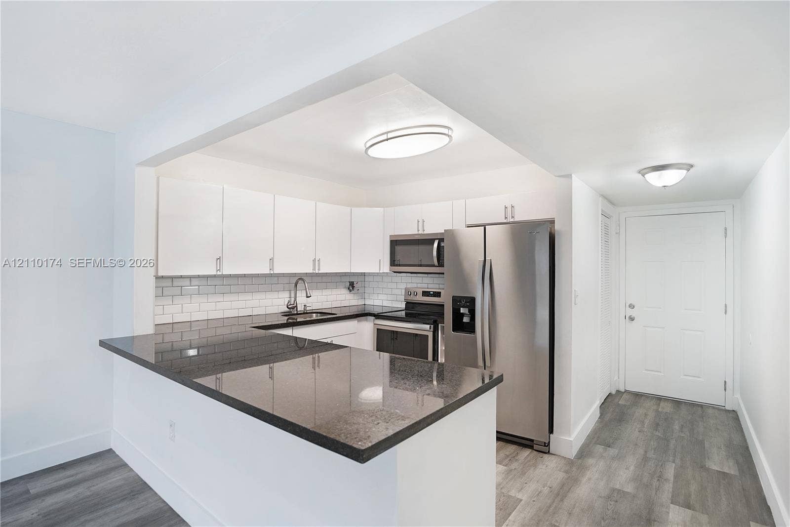 Kitchen featuring white cabinetry, dark stone countertops, stainless steel appliances, a white subway tile backsplash, and wood-finish flooring