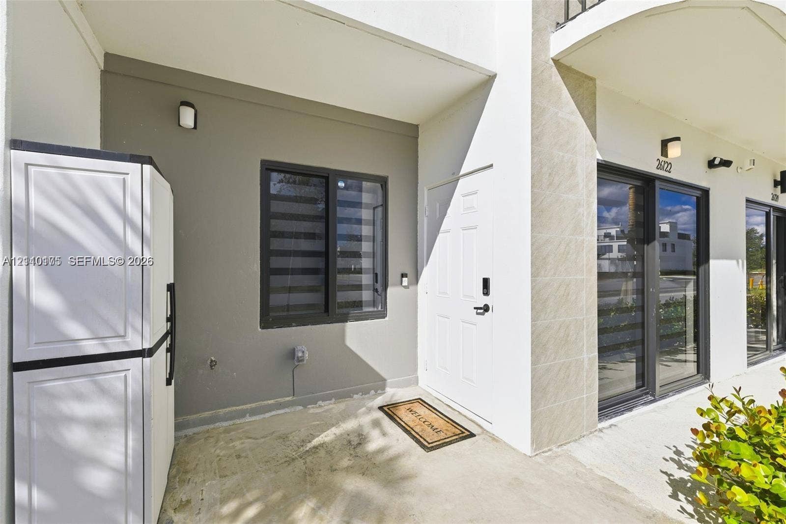 26122 SW 145th Court, #26122, Homestead, Homestead, FL 33032 Covered entryway featuring a concrete porch, neutral-toned exterior walls, modern dark-framed windows, a multi-panel entry door, and wall-mounted exterior lighting