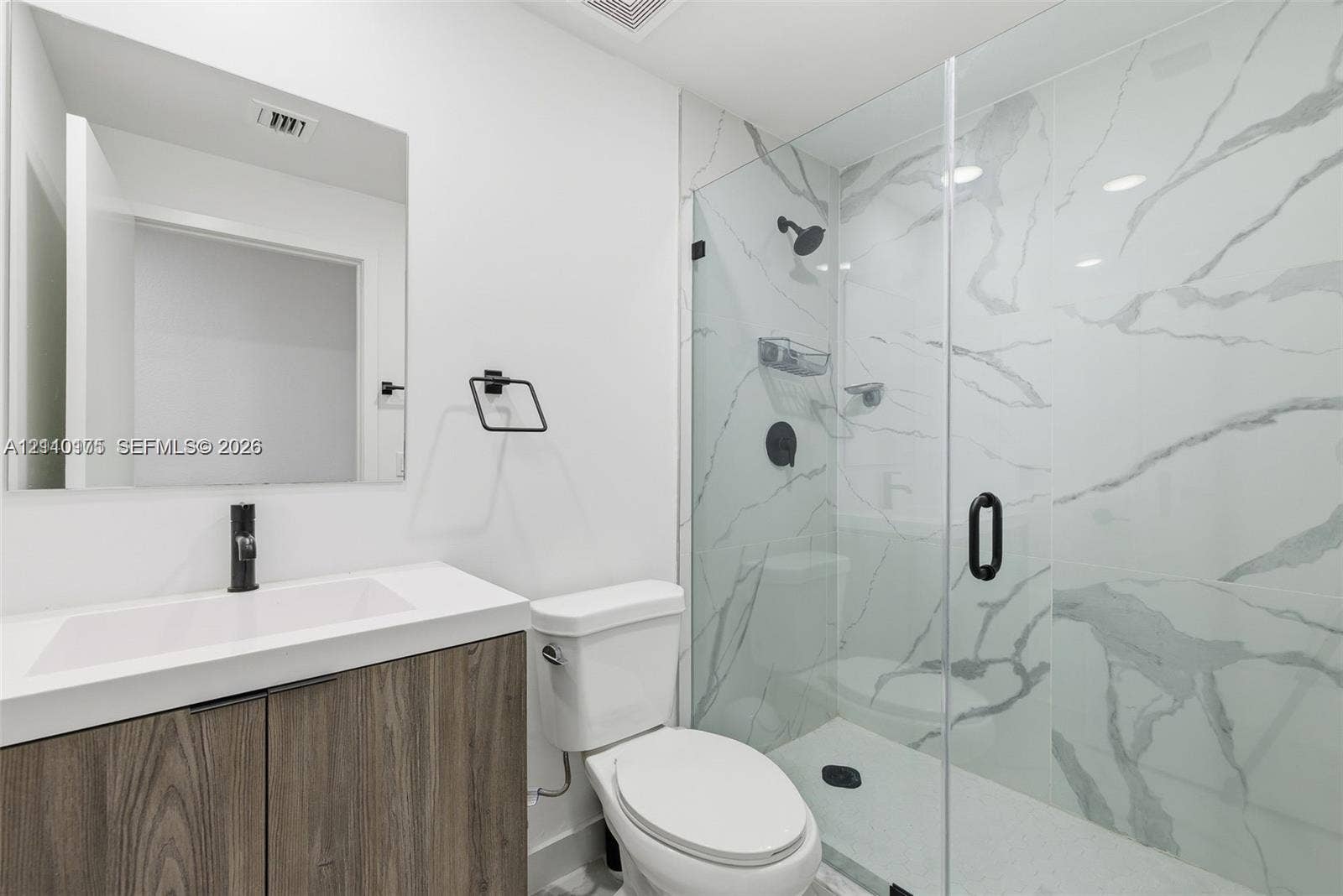 26122 SW 145th Court, #26122, Homestead, Homestead, FL 33032 Wood-finish cabinetry with a white countertop, rectangular vessel sink, wall-mounted matte black faucet, and walk-in shower with floor-to-ceiling stone-patterned tile and a frameless glass door