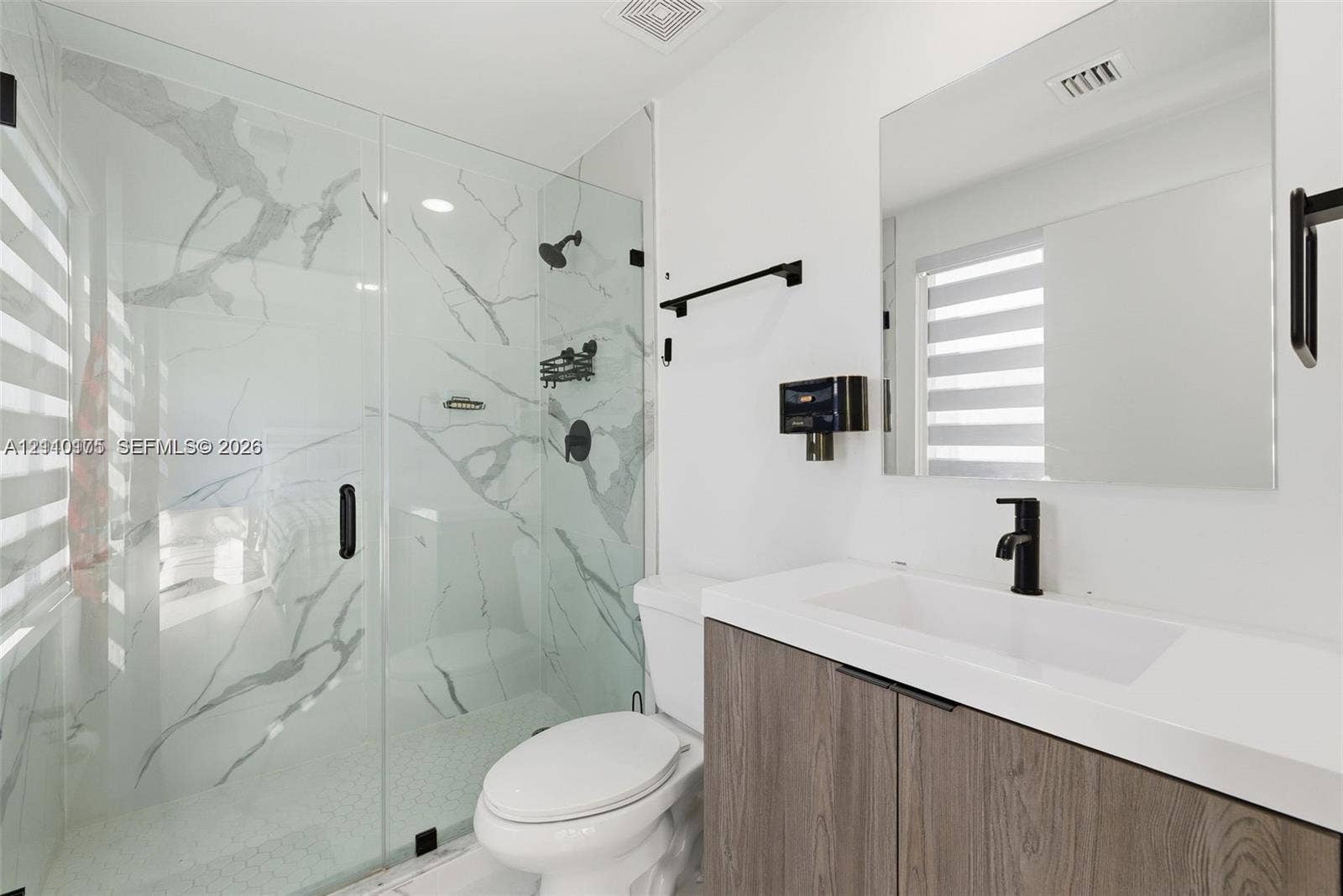 26122 SW 145th Court, #26122, Homestead, Homestead, FL 33032 Walk-in shower with stone-finish tile surround and glass enclosure, wood-finish floating vanity with white countertop, matte black fixtures, and large frameless mirror