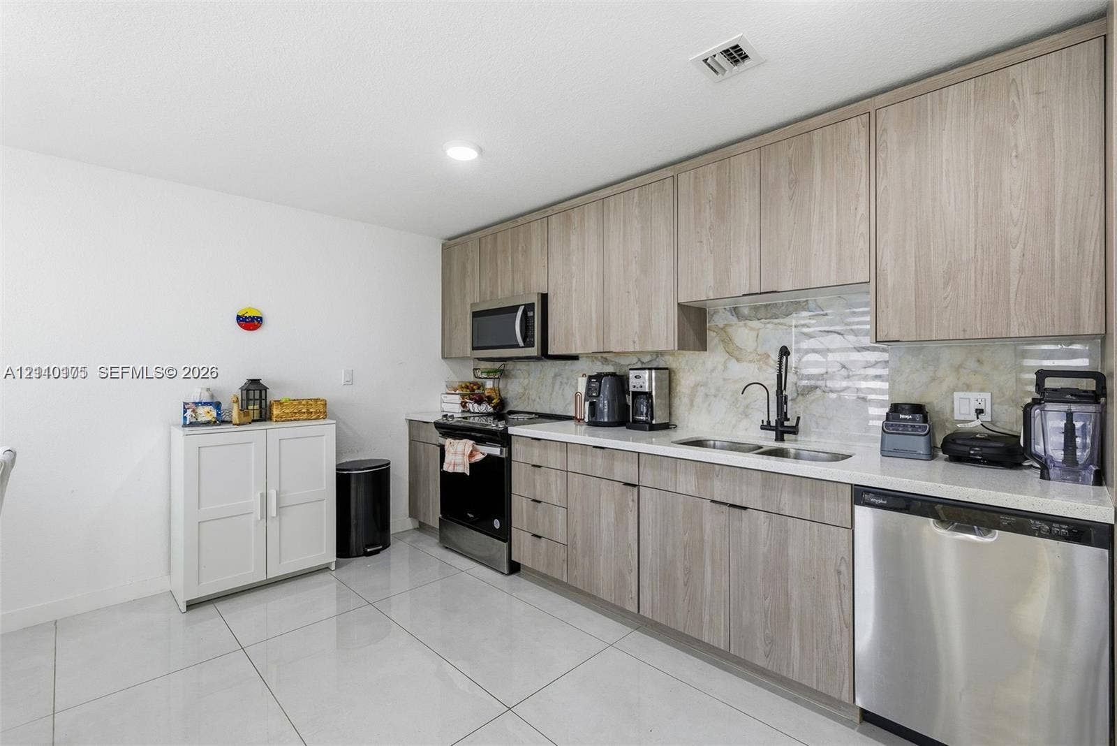 26122 SW 145th Court, #26122, Homestead, Homestead, FL 33032 Kitchen featuring flat-panel wood-finish cabinetry, light-toned stone-surface countertops, stone tile backsplash, stainless steel appliances, and large-format porcelain tile flooring