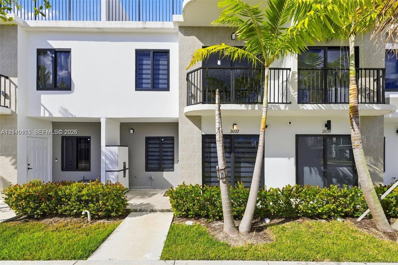 26122 SW 145th Court, #26122, Homestead, Homestead, FL 33032 Two-story townhome exterior featuring a private second-level balcony with black metal railings, smooth stucco finish, dark-framed multi-pane windows, and integrated wall-mounted exterior lighting