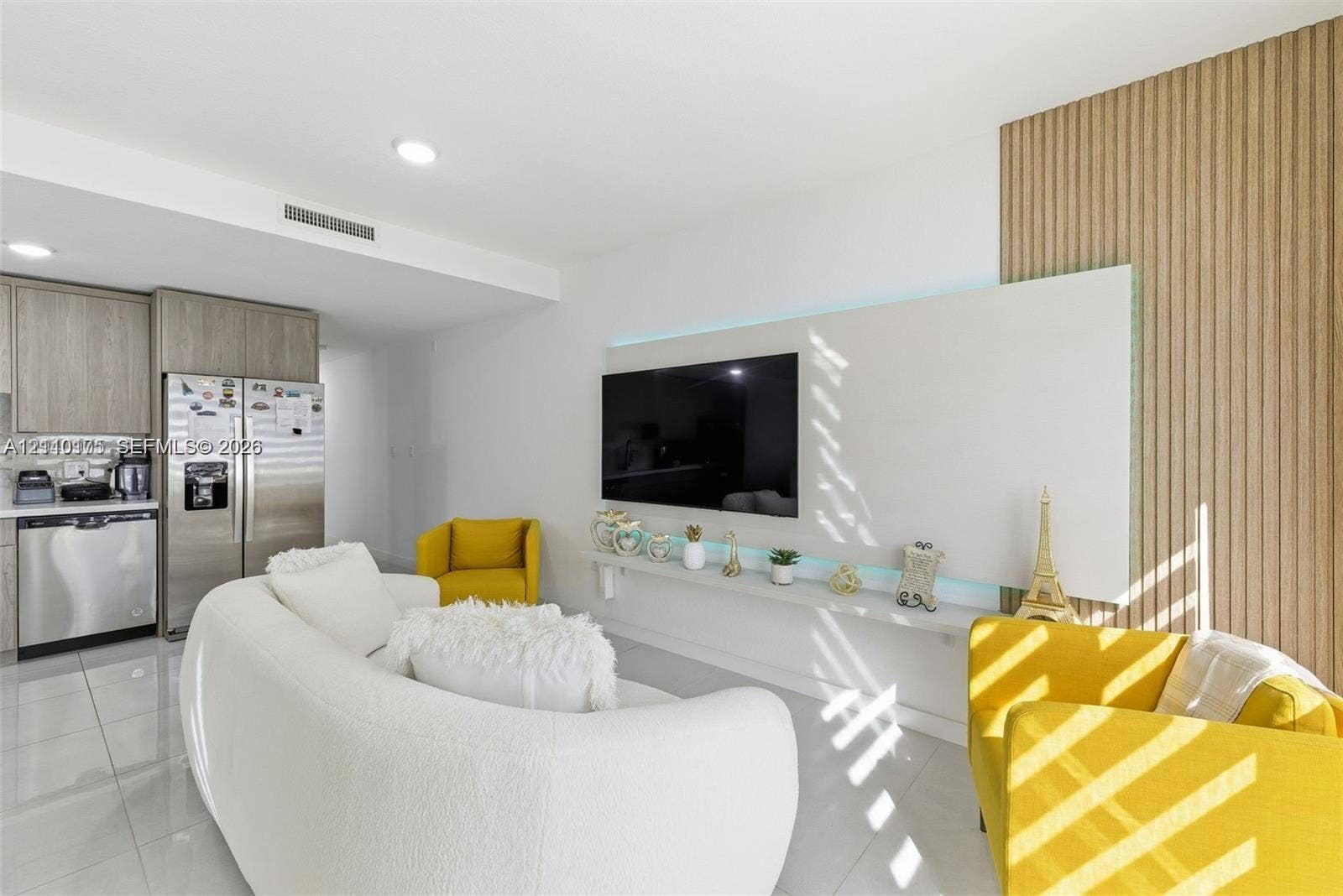 26122 SW 145th Court, #26122, Homestead, Homestead, FL 33032 Modern interior featuring white tile flooring, custom slatted wood wall paneling, a minimalist built-in wall-mounted display shelf with integrated lighting, and stainless steel kitchen appliances