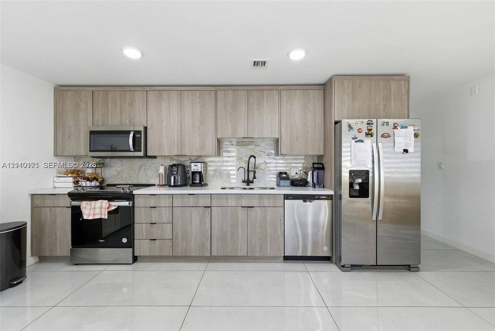 26122 SW 145th Court, #26122, Homestead, Homestead, FL 33032 Kitchen featuring wood-finish cabinetry, light-toned stone-style backsplash, integrated stainless steel appliances, and large-format tile flooring