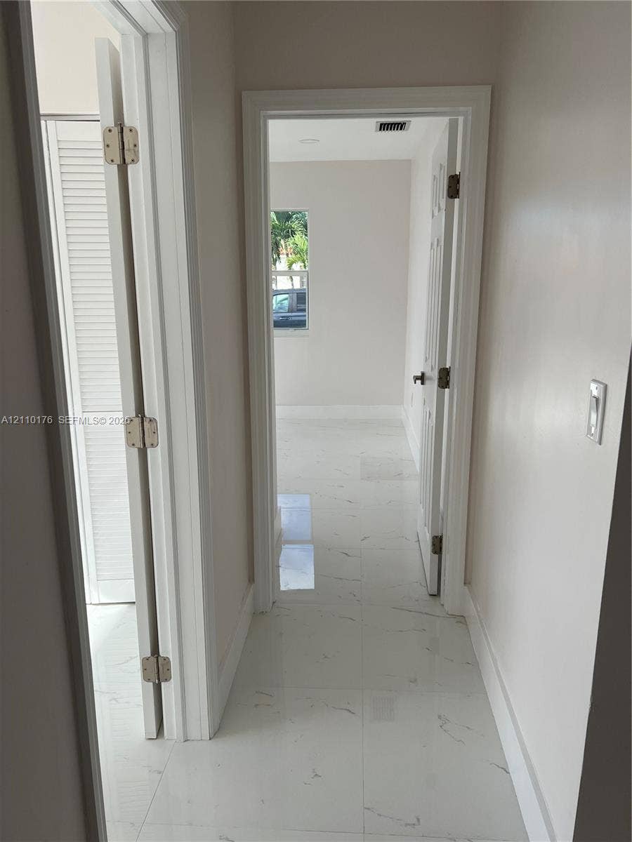 Hallway featuring light-colored stone-finish tile flooring, white interior doors with brushed metal hardware, and louvered closet doors