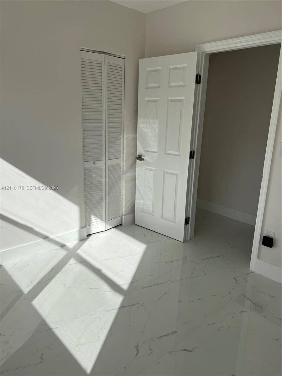 Polished stone-finish flooring with veining detail, white six-panel interior door with matte black hardware, and floor-to-ceiling white louvered closet doors