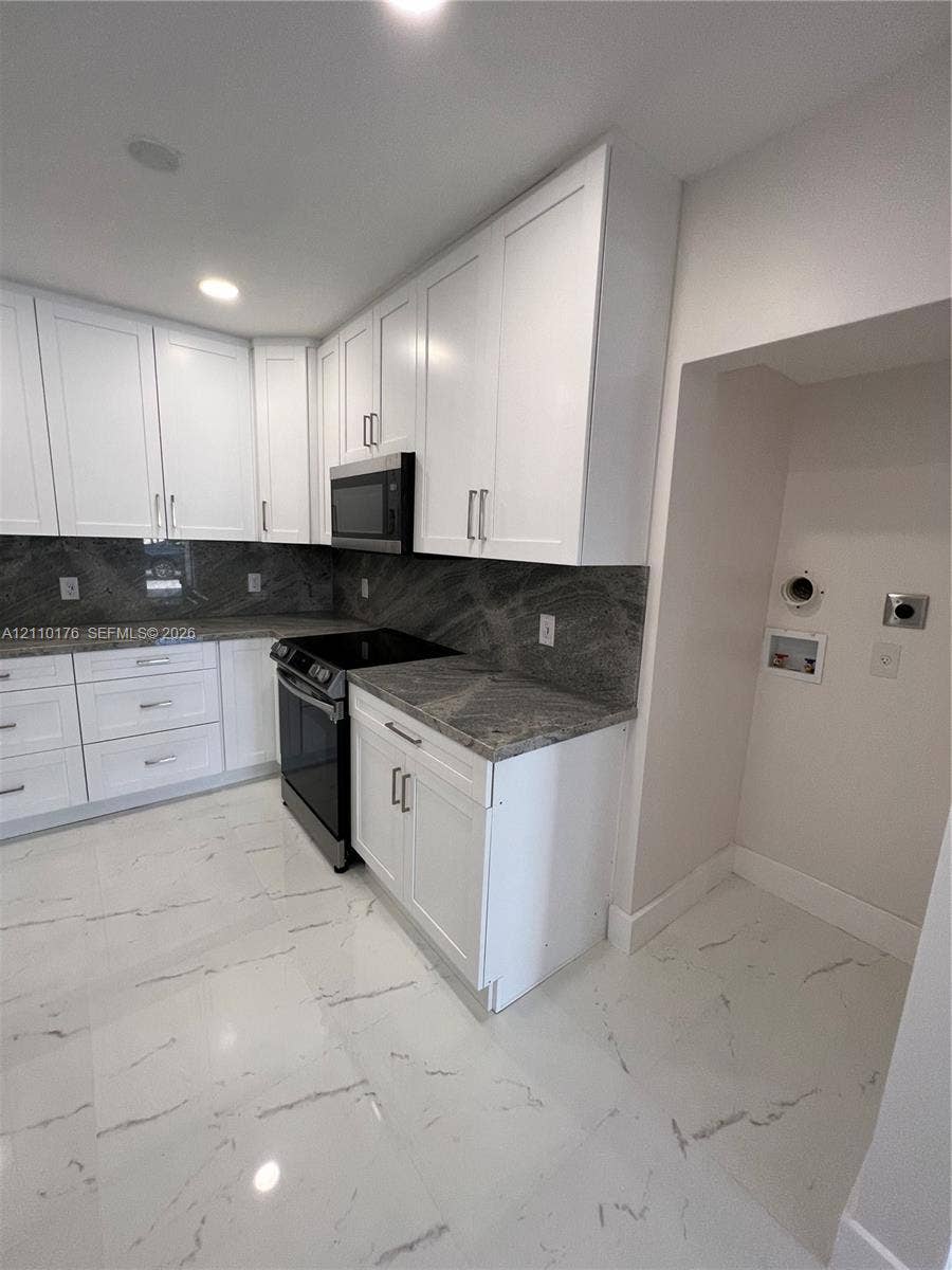 Kitchen featuring white shaker-style cabinetry, stone countertops, stone backsplash, stainless steel appliances, and large-format tile flooring