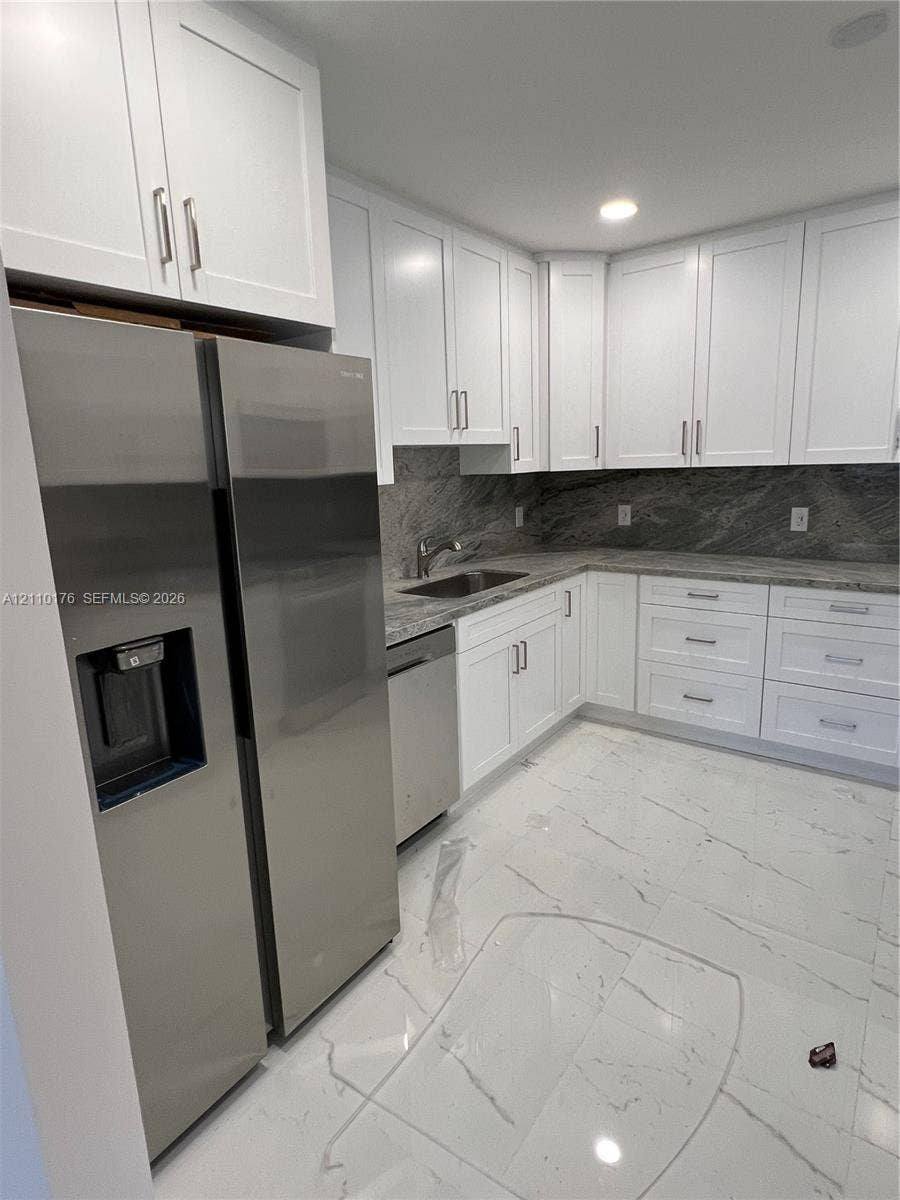 Kitchen featuring white shaker-style cabinetry, stainless steel appliances, stone countertops, stone tile backsplash, and polished stone-finish flooring