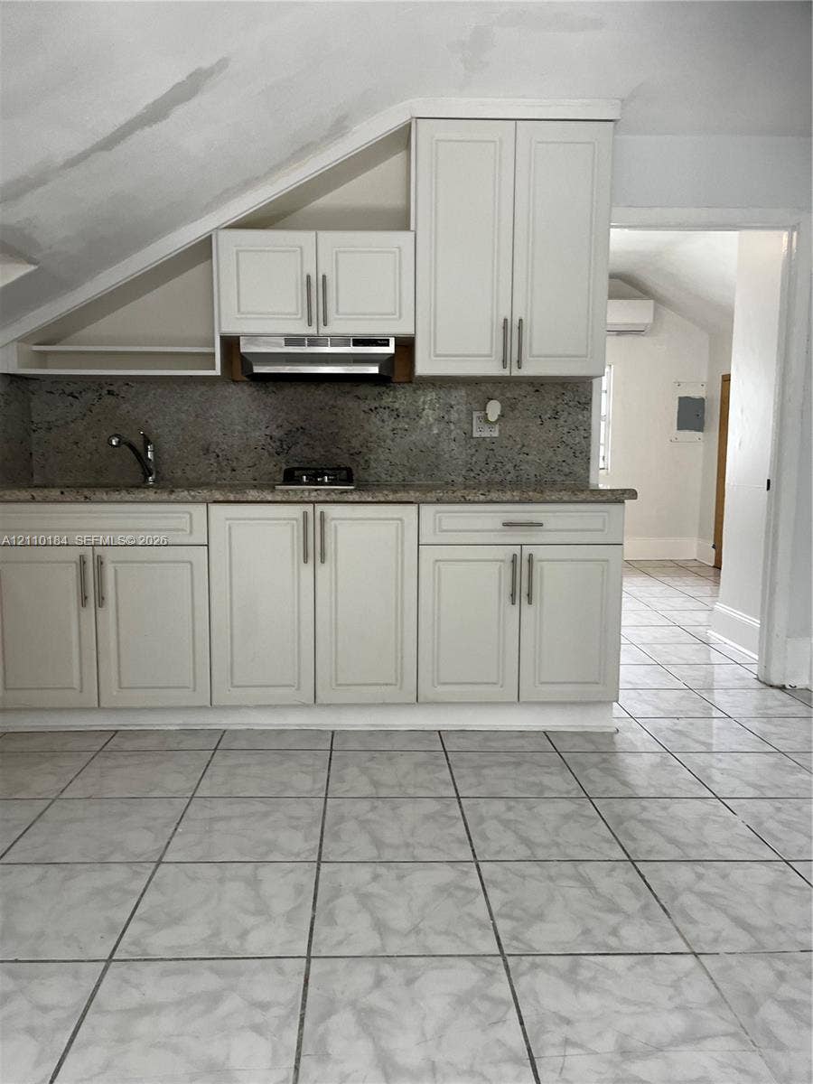 Kitchen featuring white shaker-style cabinetry, stone-finish countertops, tile flooring, and a stainless steel range hood