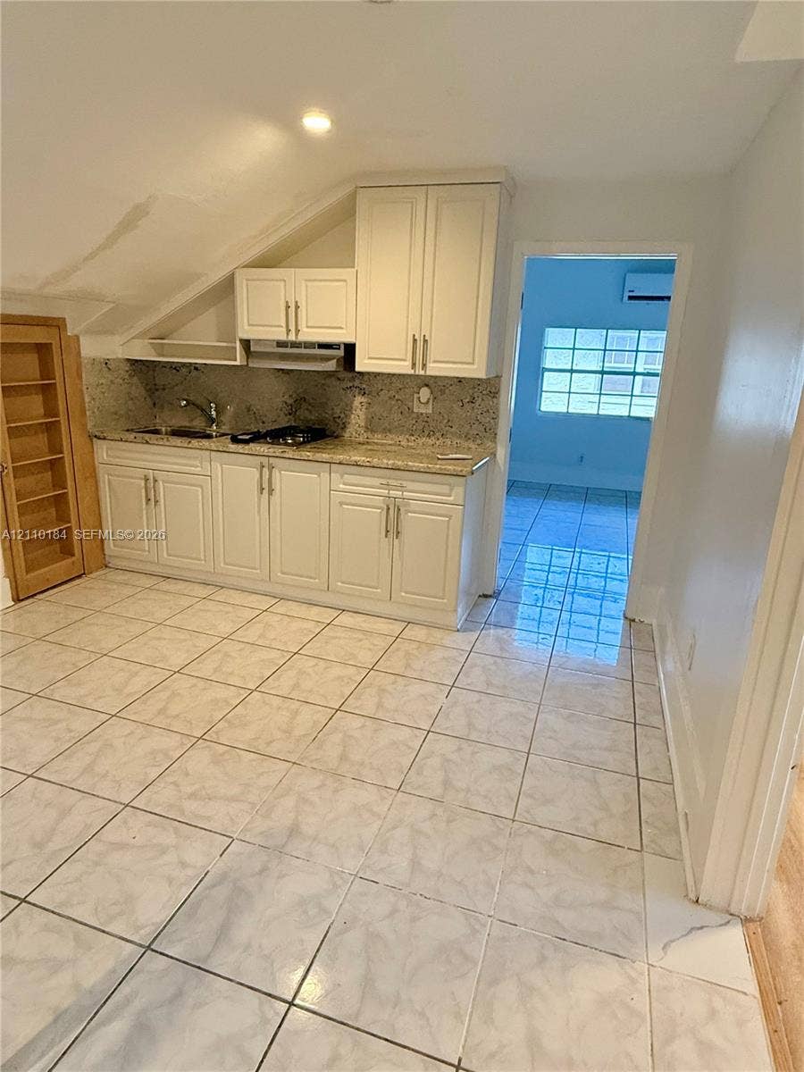 Kitchen area featuring shaker-style white cabinetry, stone-finish countertops, tile flooring, and integrated built-in shelving