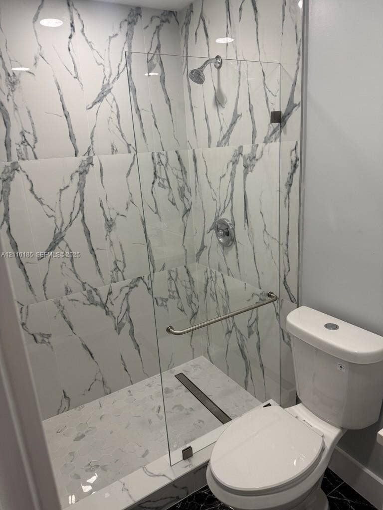 2596 Rosehaven Road, #2, West Palm Beach, West Palm Beach, FL 33415 Walk-in shower featuring floor-to-ceiling veined tile, frameless glass enclosure, polished metal hardware, and linear drain