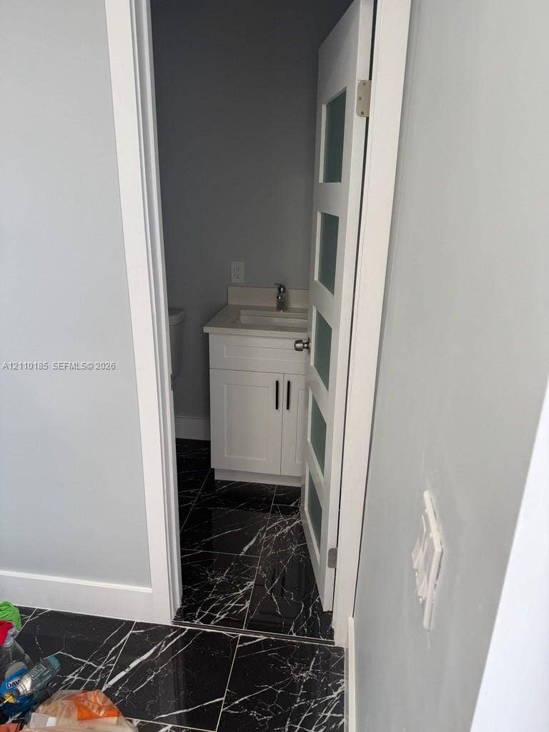 2596 Rosehaven Road, #2, West Palm Beach, West Palm Beach, FL 33415 Interior space featuring high-contrast black veined tile flooring, a white vanity cabinet with shaker-style doors, and a door paneled with frosted glass inserts