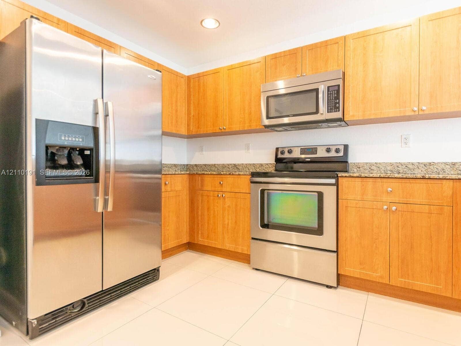 8999 NW 107 Court, #218-1, Miami, Miami, FL 33178 Kitchen featuring natural wood-finish cabinetry, speckled stone countertops, and stainless steel appliances including a double-door refrigerator, over-the-range microwave, and slide-in range with large-format floor tile