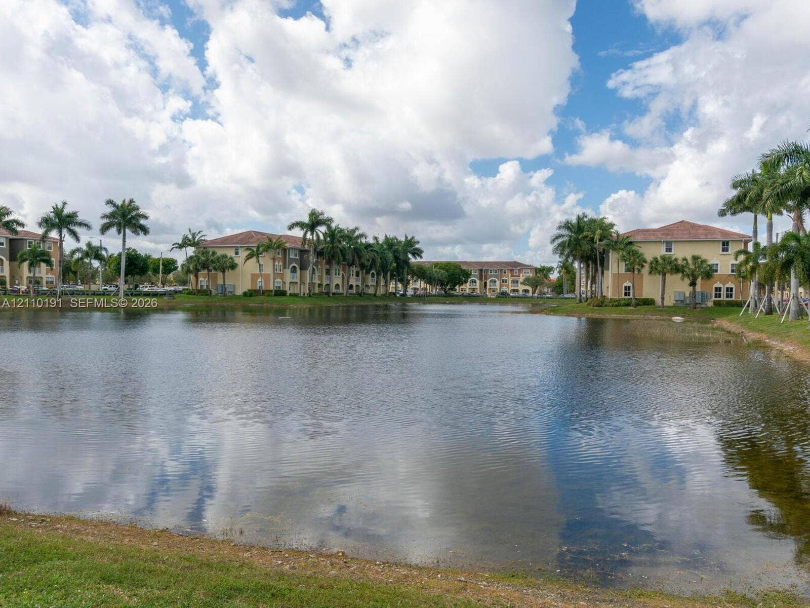 8999 NW 107 Court, #218-1, Miami, Miami, FL 33178 Waterfront setting featuring a central pond, exterior buildings with terracotta-style roof tiles, and mature palm tree landscaping