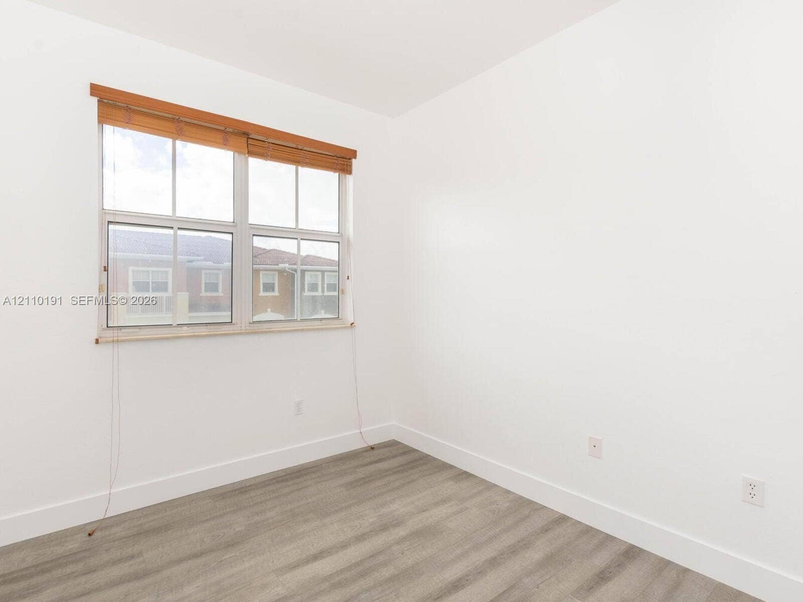 8999 NW 107 Court, #218-1, Miami, Miami, FL 33178 Neutral-toned interior space featuring wood-finish flooring, crisp white walls, and a multi-pane window with wood-slat blinds