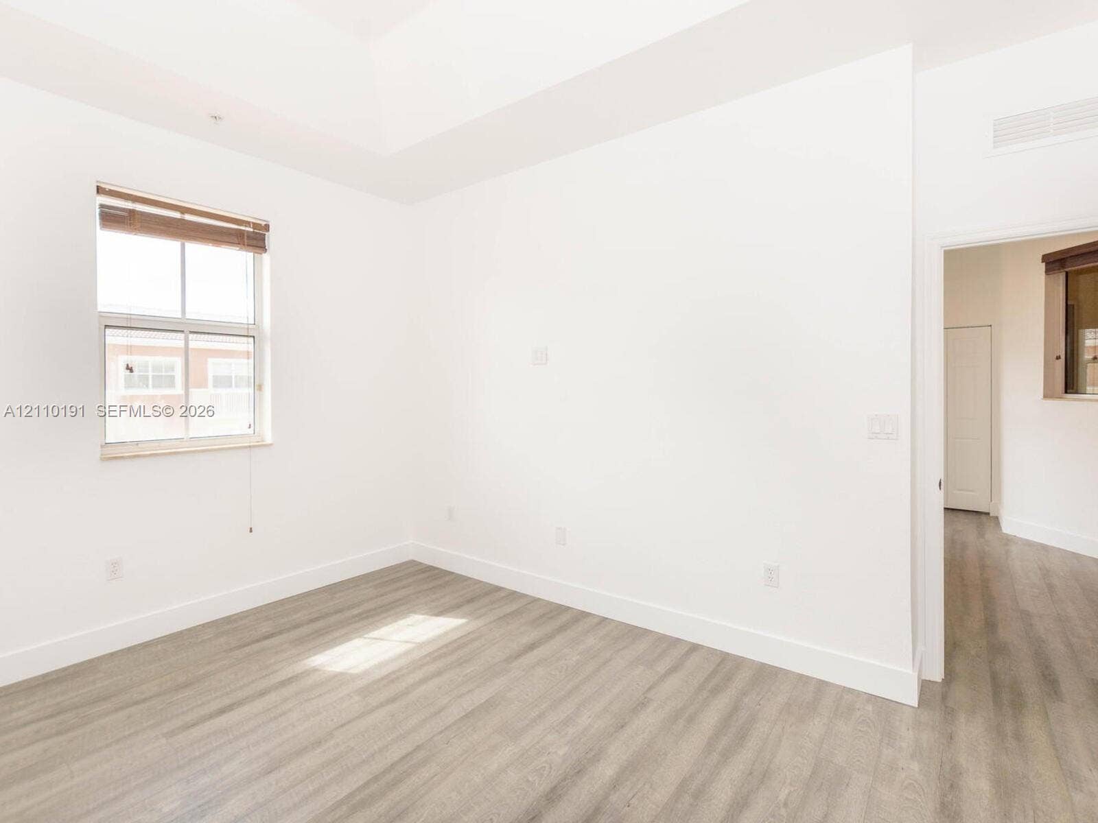 8999 NW 107 Court, #218-1, Miami, Miami, FL 33178 Neutral-toned room featuring a tray ceiling, wood-finish flooring, and a window with blinds