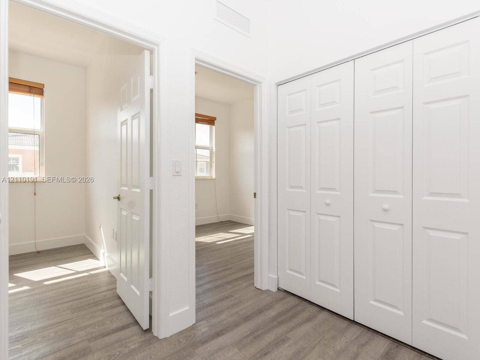 8999 NW 107 Court, #218-1, Miami, Miami, FL 33178 Hallway featuring wood-finish flooring, two sets of white paneled bifold closet doors, and interior paneled doors