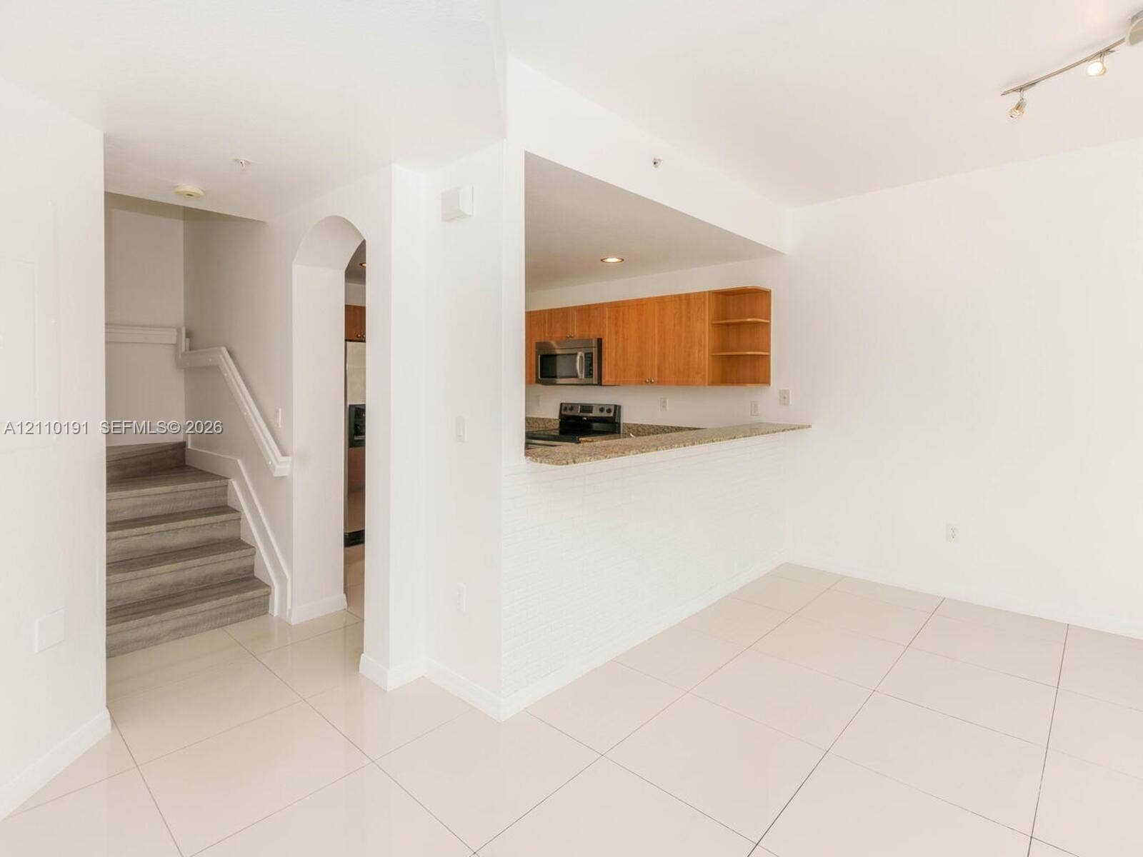 8999 NW 107 Court, #218-1, Miami, Miami, FL 33178 Kitchen featuring flat-panel wood cabinetry, stone-finish countertops, and stainless steel built-in appliances, complemented by a stone-tile floor and a structural arched entryway