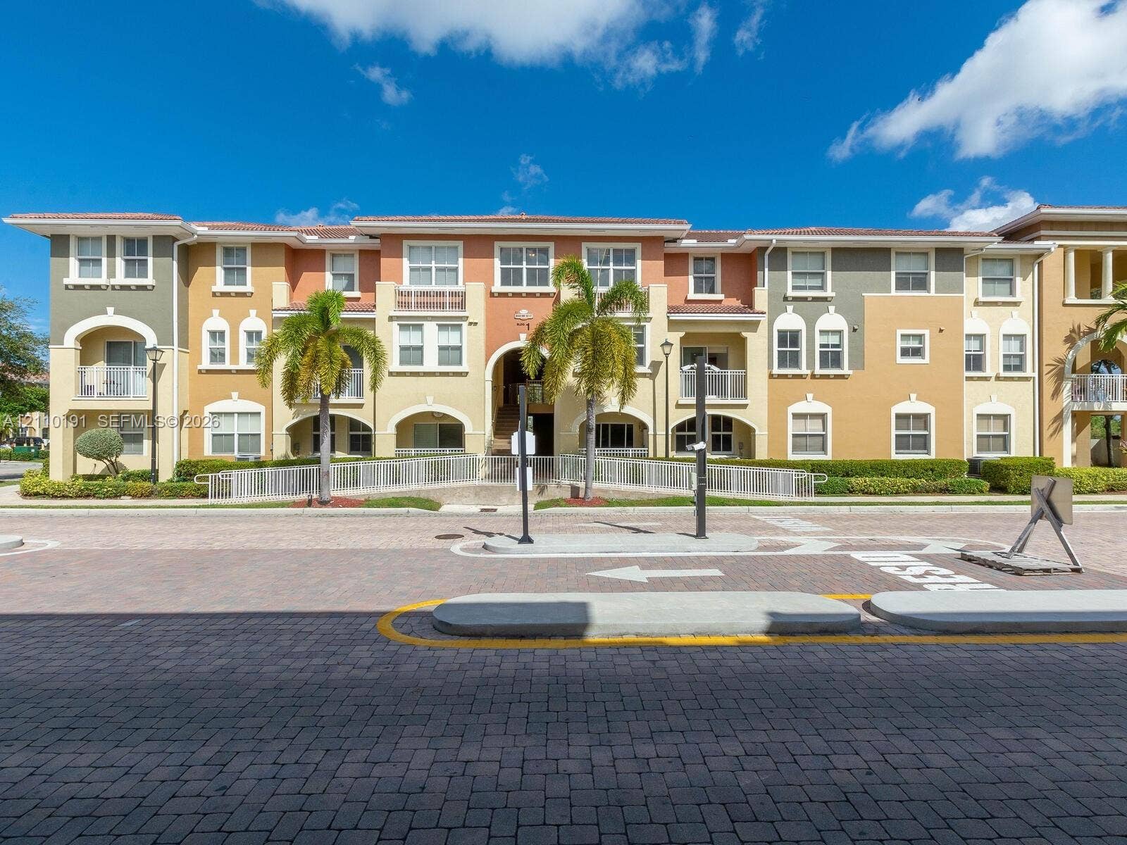 8999 NW 107 Court, #218-1, Miami, Miami, FL 33178 Multi-story Mediterranean-style exterior featuring a stucco facade, arched architectural detailing, private balconies with metal railings, and integrated palm tree landscaping