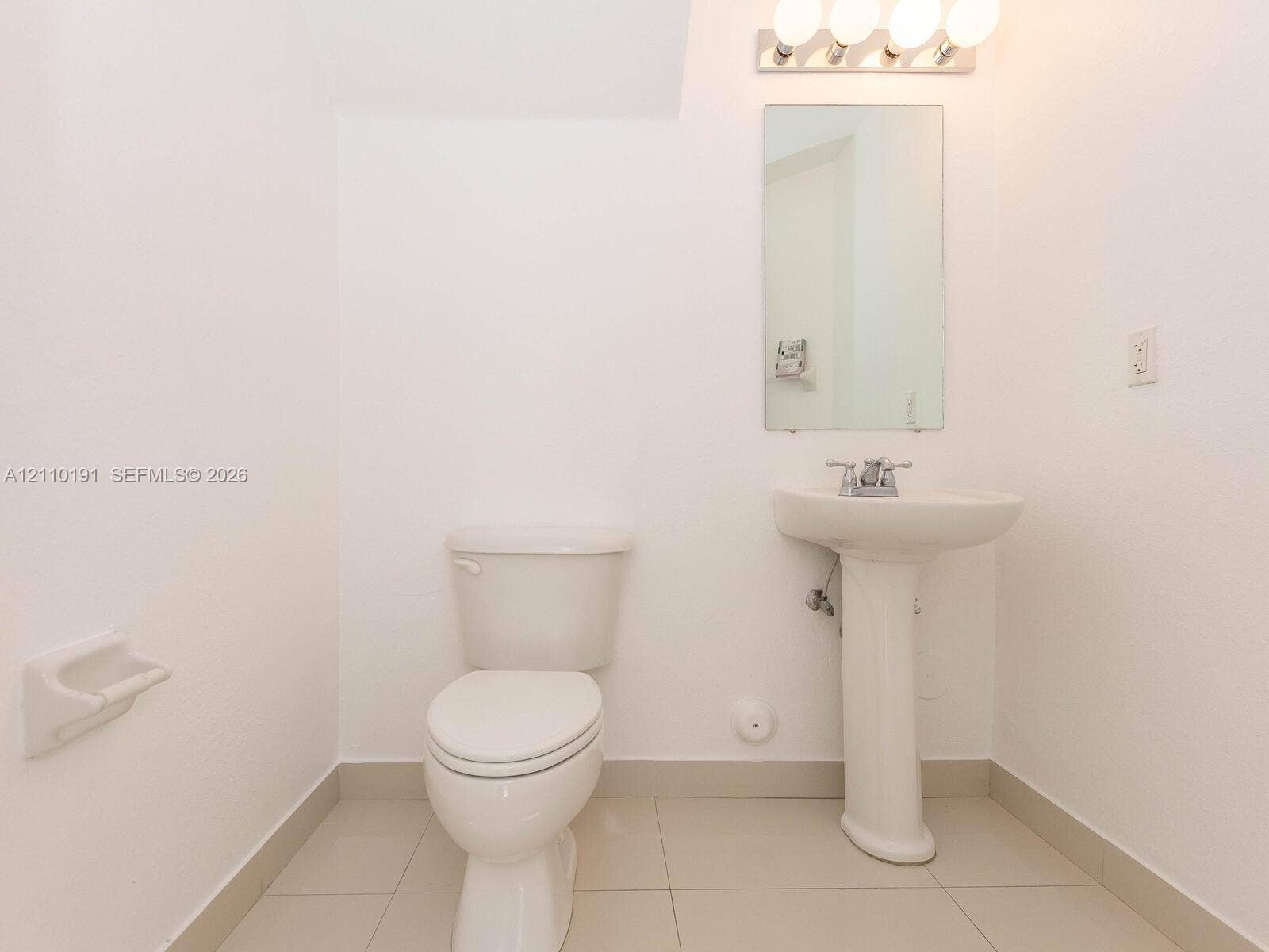 8999 NW 107 Court, #218-1, Miami, Miami, FL 33178 Pedestal sink with chrome faucet, wall-mounted rectangular mirror, four-bulb vanity lighting, and ceramic tile flooring