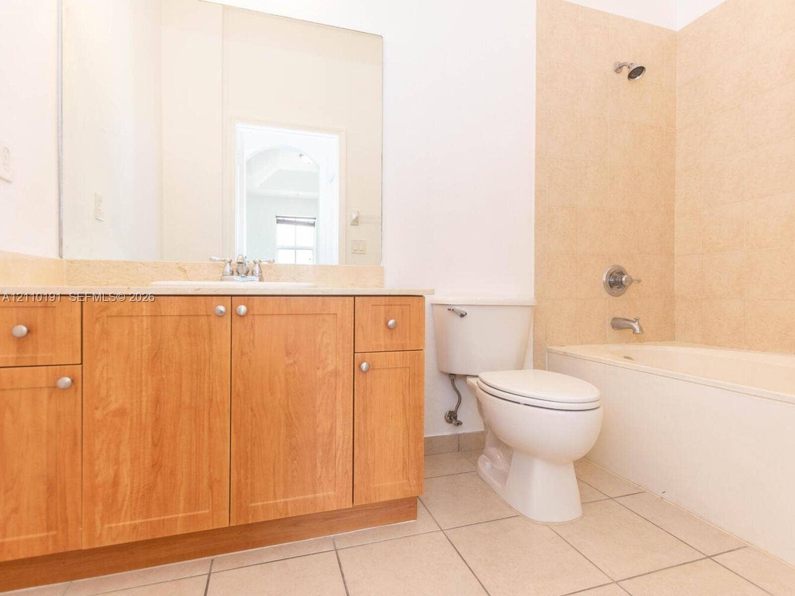 8999 NW 107 Court, #218-1, Miami, Miami, FL 33178 Bathroom featuring wood-finish cabinetry, a neutral stone countertop with an integrated basin, a wall-to-wall vanity mirror, ceramic tile flooring, and a tub-shower combination with tiled surround