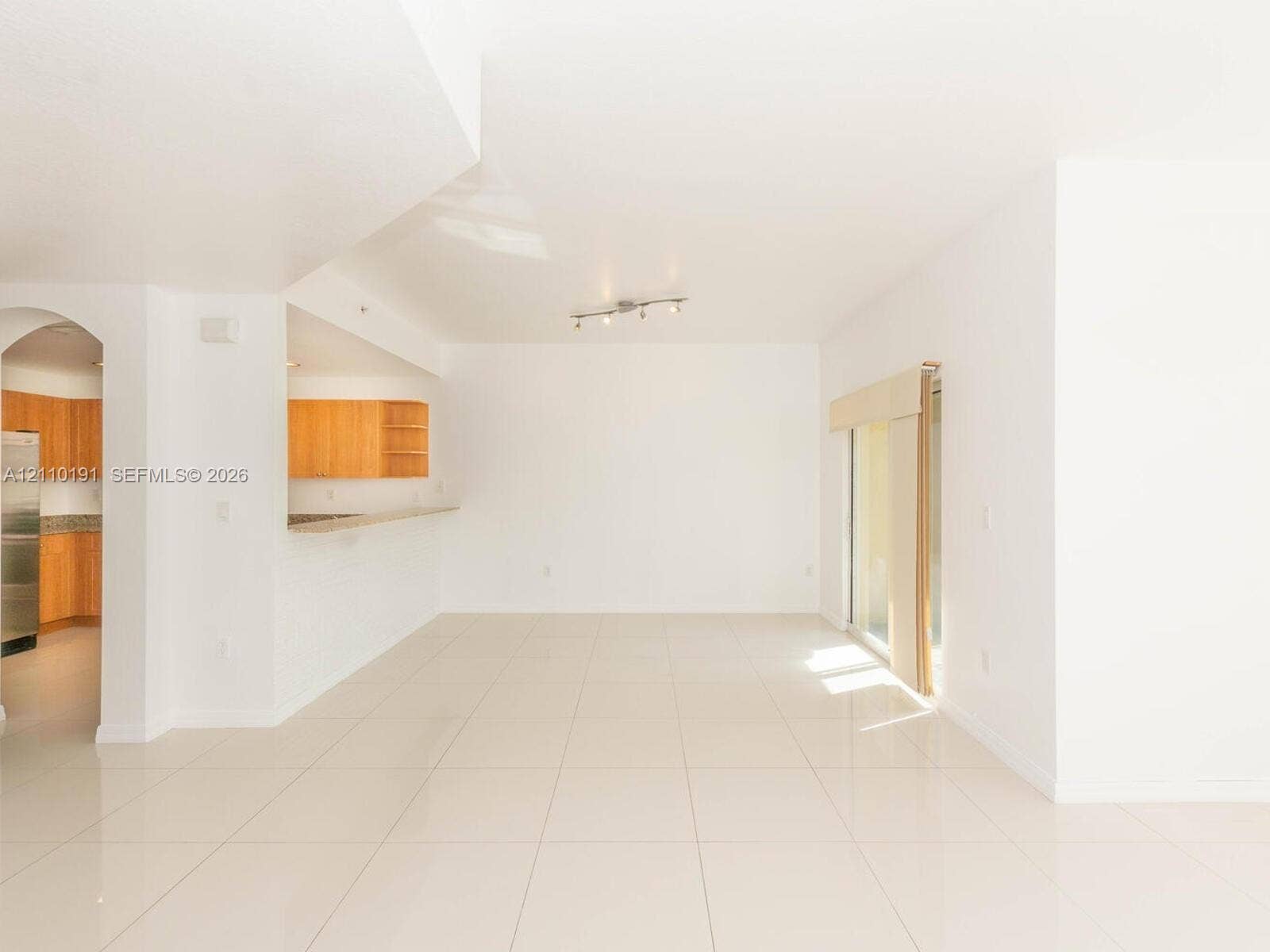 8999 NW 107 Court, #218-1, Miami, Miami, FL 33178 Open-concept interior featuring large-format tile flooring, arched architectural detail, sliding glass doors, and a breakfast bar with wood-toned cabinetry